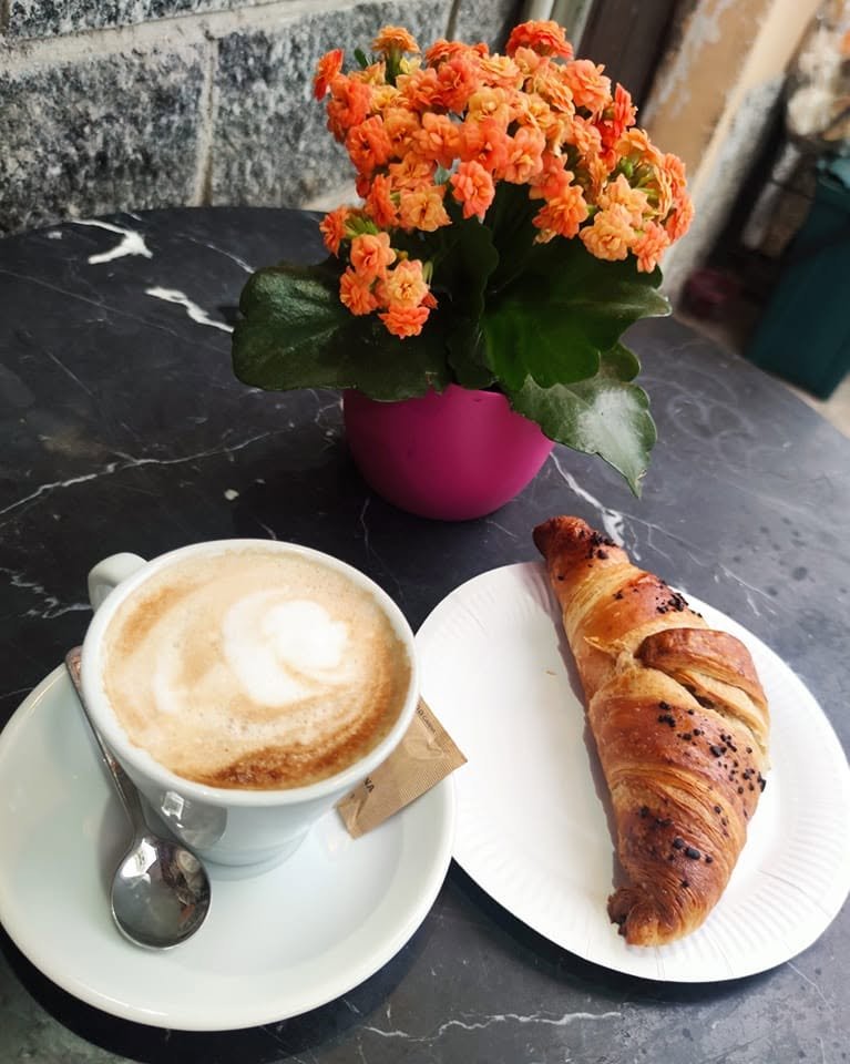 Cappuccino con latte art e cornetto con granella di cioccolato su tavolino in marmo nero accanto a fiori arancioni